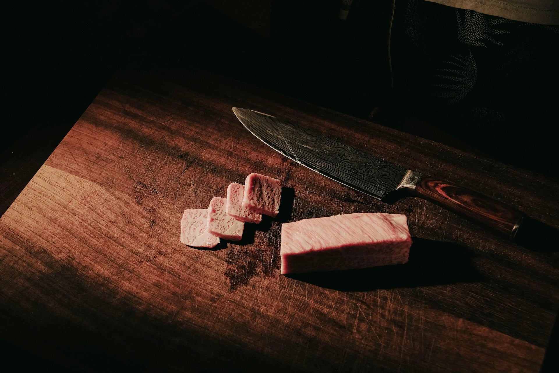 Uppskuret kött och kockkniv på skärbräda i trä i mörk stämningsfull miljö